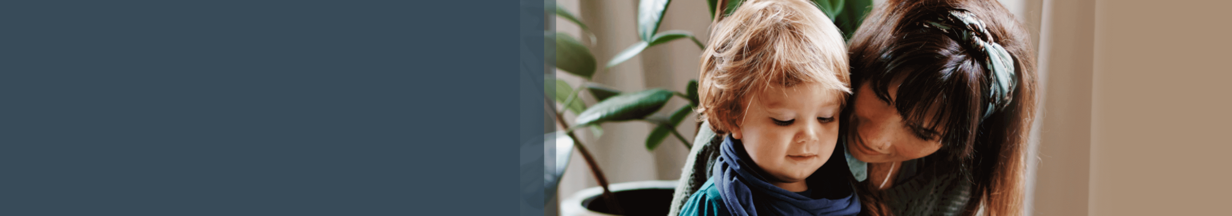 W pokoju, na tle figowca, kobieta siedząc na pufie czyta dziecku